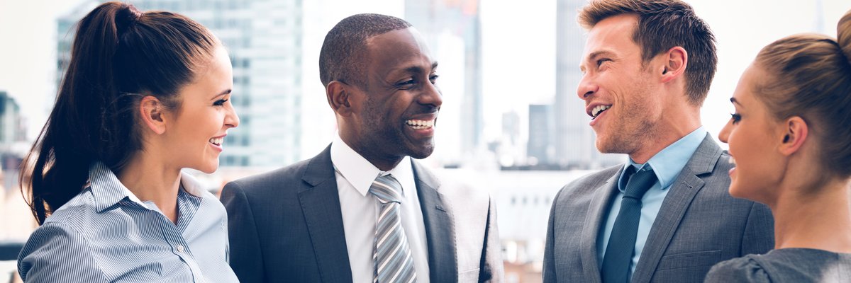 Four friends in business attire stand outside and laugh.