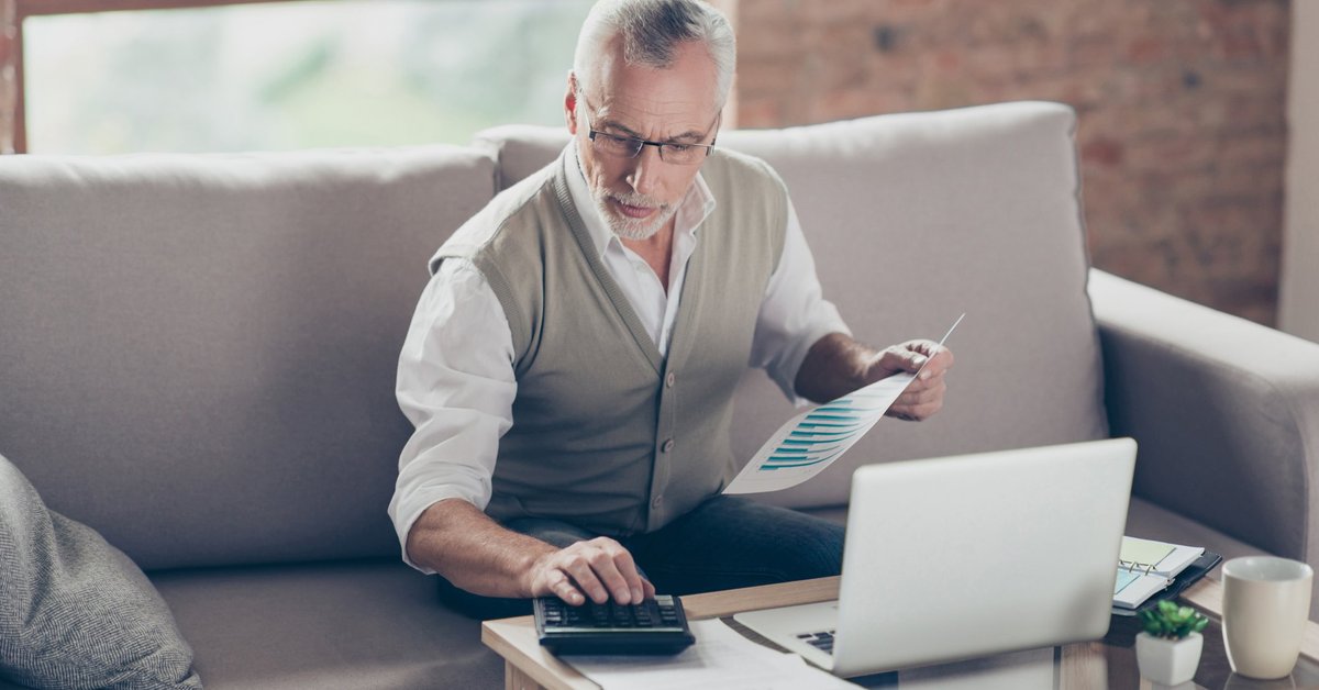 Older man using calculator and laptop.