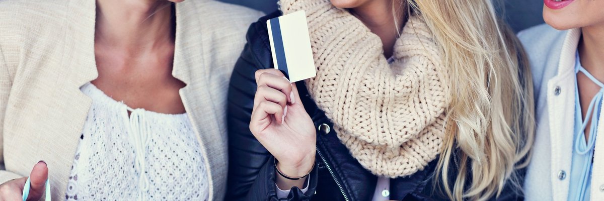 Three women holding shopping bags, one holding a credit card