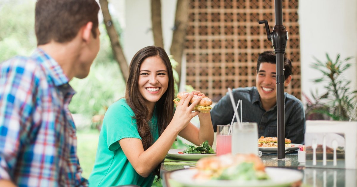 Friends sitting outdoors eating sub sandwiches.