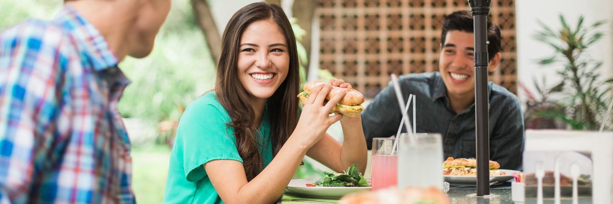 Friends sitting outdoors eating sub sandwiches.