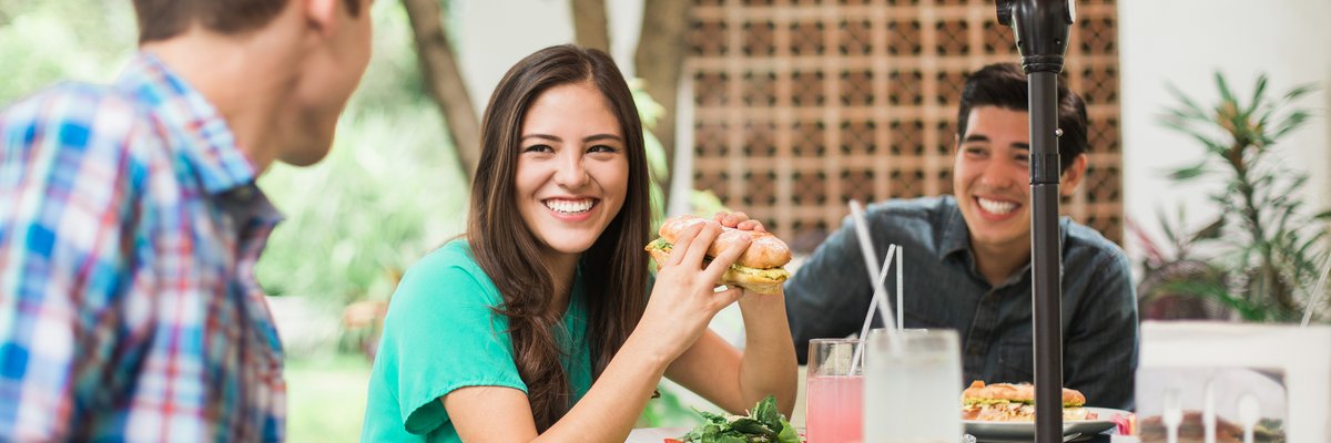 Friends sitting outdoors eating sub sandwiches.