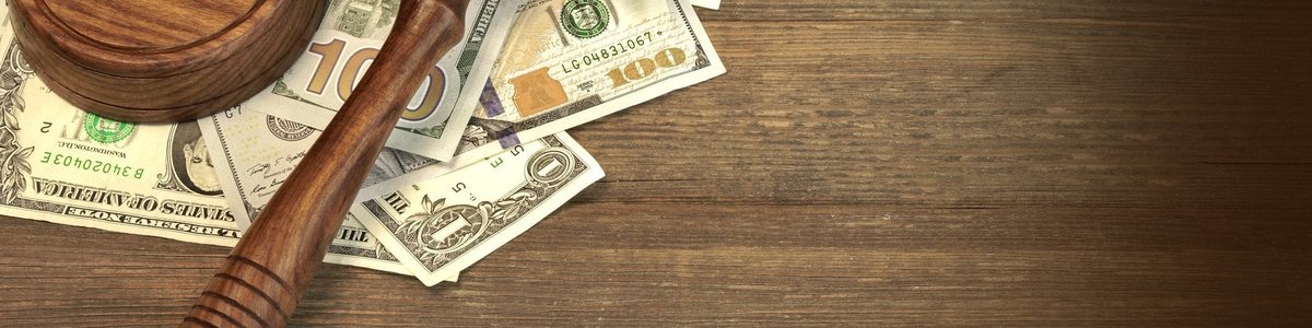 A wooden gavel on top of a messy pile of cash on a desk.