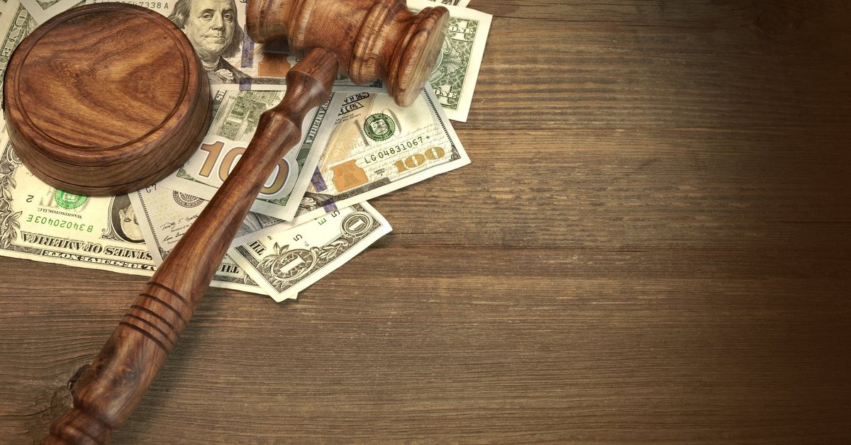 A wooden gavel on top of a messy pile of cash on a desk.