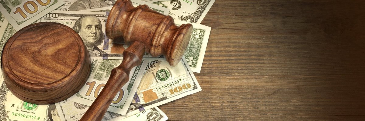 A wooden gavel on top of a messy pile of cash on a desk.