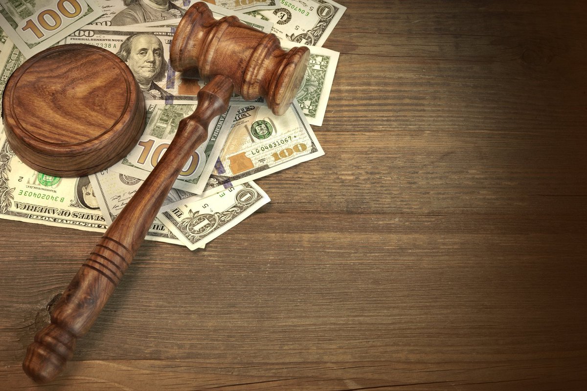A wooden gavel on top of a messy pile of cash on a desk.