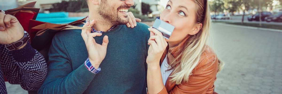 Man Laughing And Holding Shopping Bags As Girlfriend Holds Credit Card And Smirks