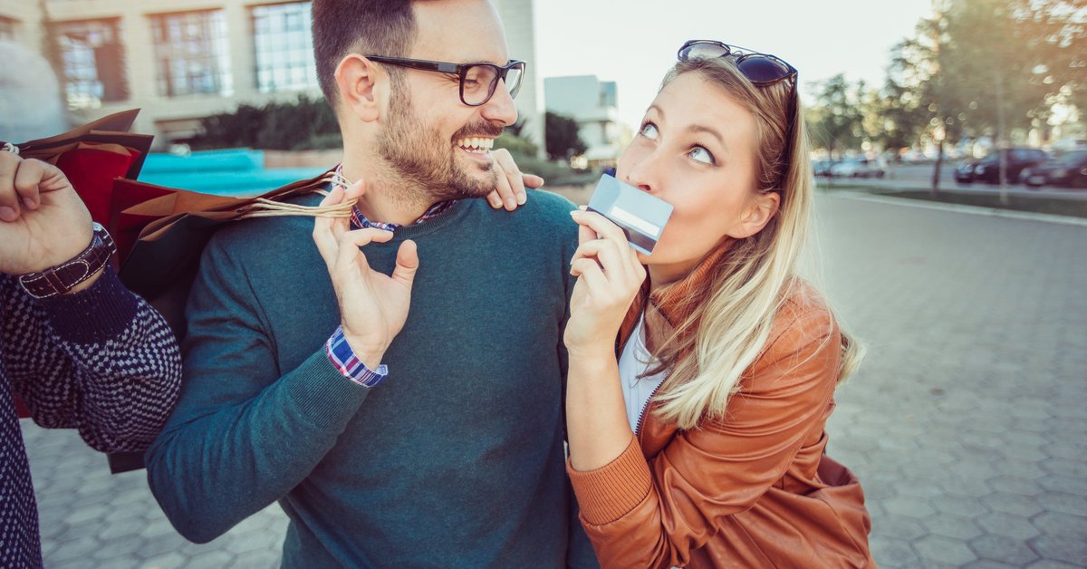 Man Laughing And Holding Shopping Bags As Girlfriend Holds Credit Card And Smirks
