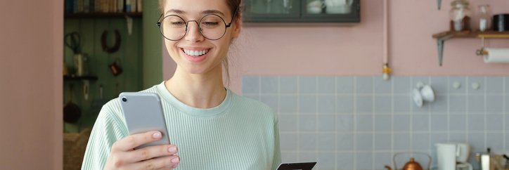 Smiling girl in kitchen with credit card and phone.