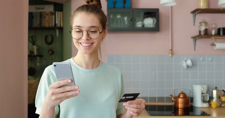 Smiling girl in kitchen with credit card and phone.