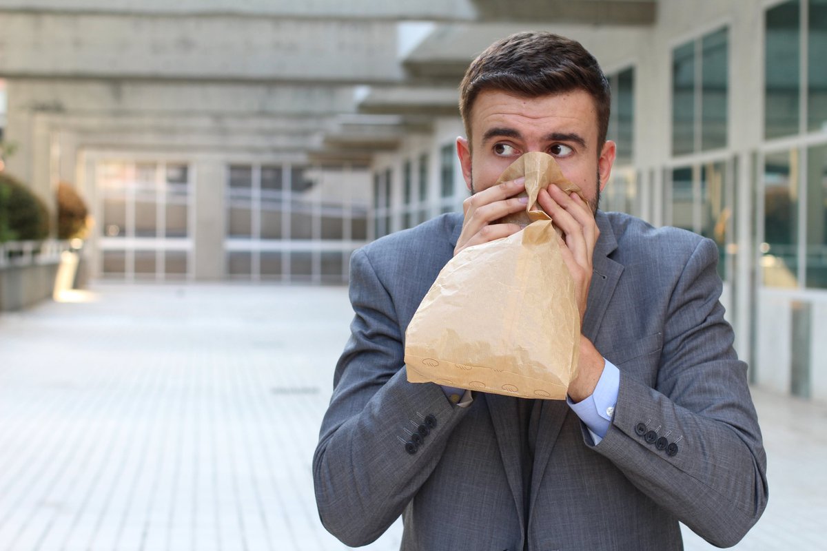 Young man in suit hyperventilating into paper bag.