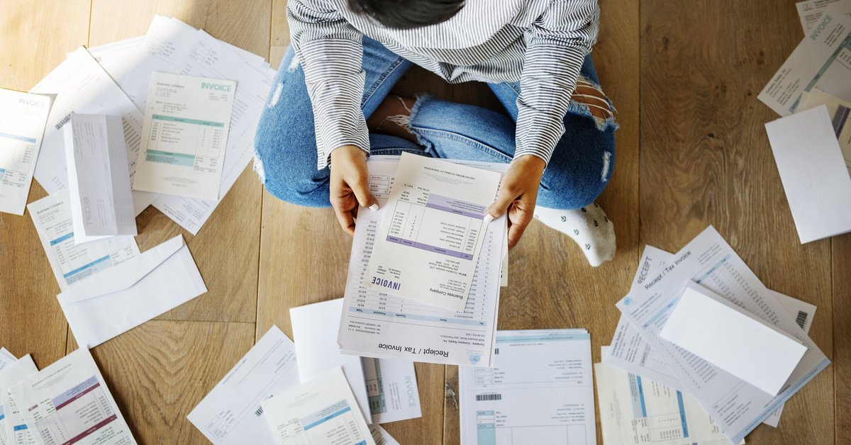 Man sitting on floor surrounded by bills.