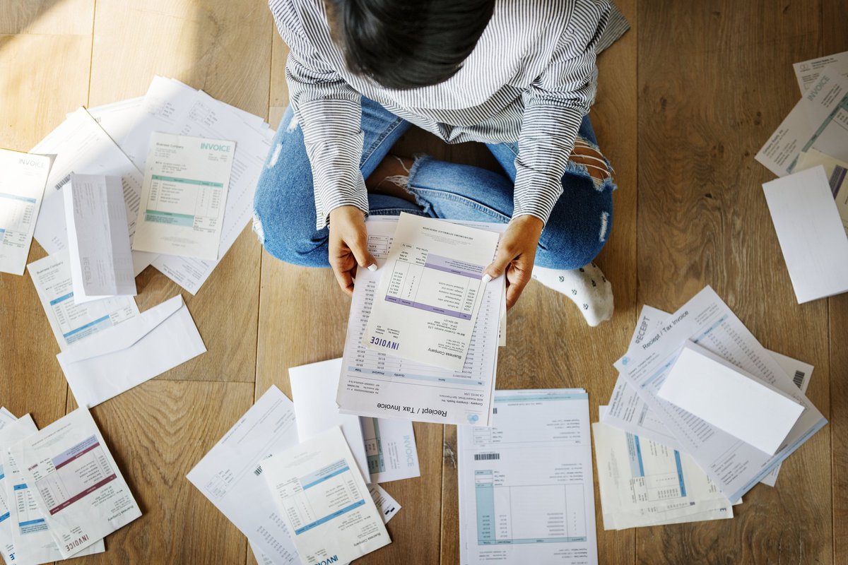 Man sitting on floor surrounded by bills.