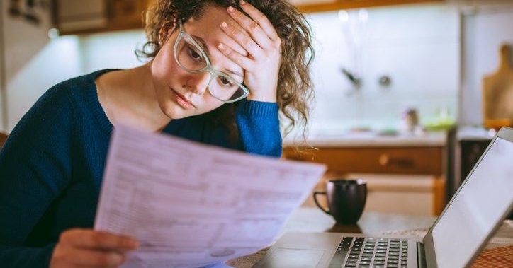 Young woman looks at her bills with a worried facial expression.