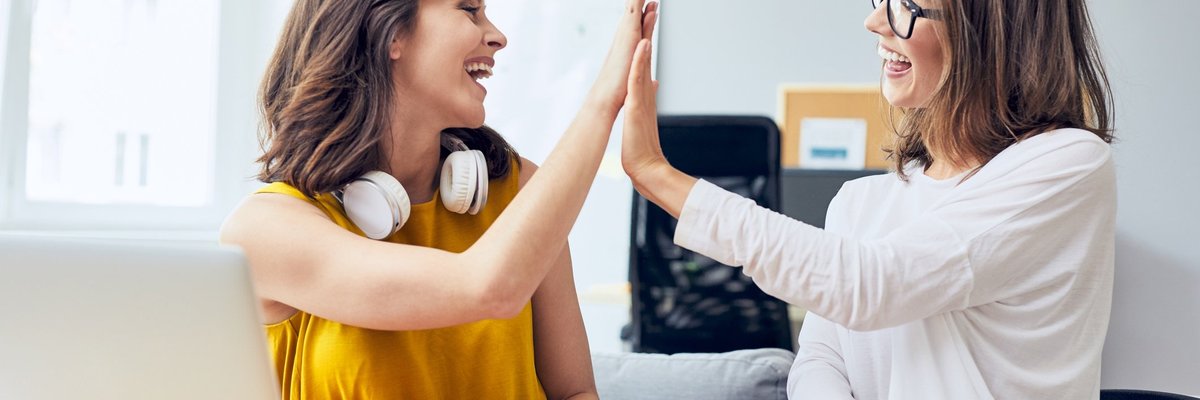 two women high fiving in front of a laptop