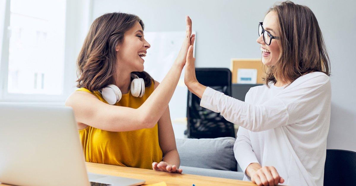 two women high fiving in front of a laptop