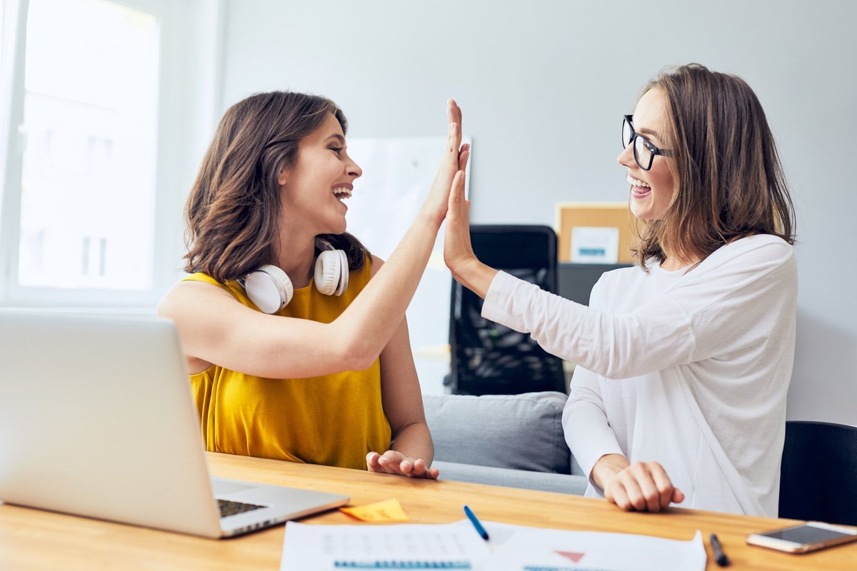 two women high fiving in front of a laptop