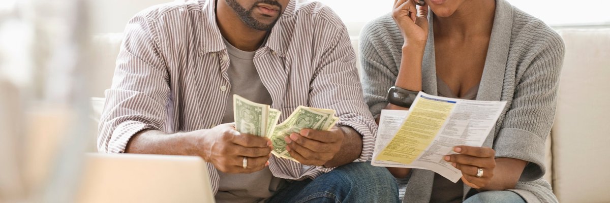 A couple pays bills on the phone and with cash at home.