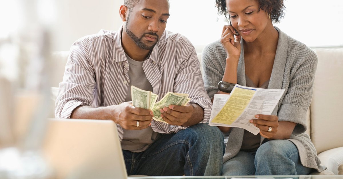 A couple pays bills on the phone and with cash at home.