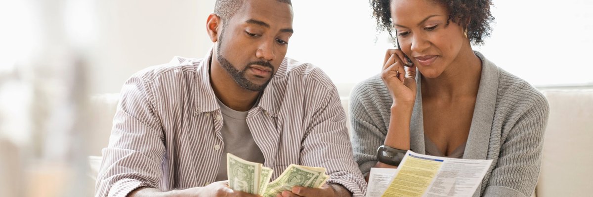 A couple pays bills on the phone and with cash at home.