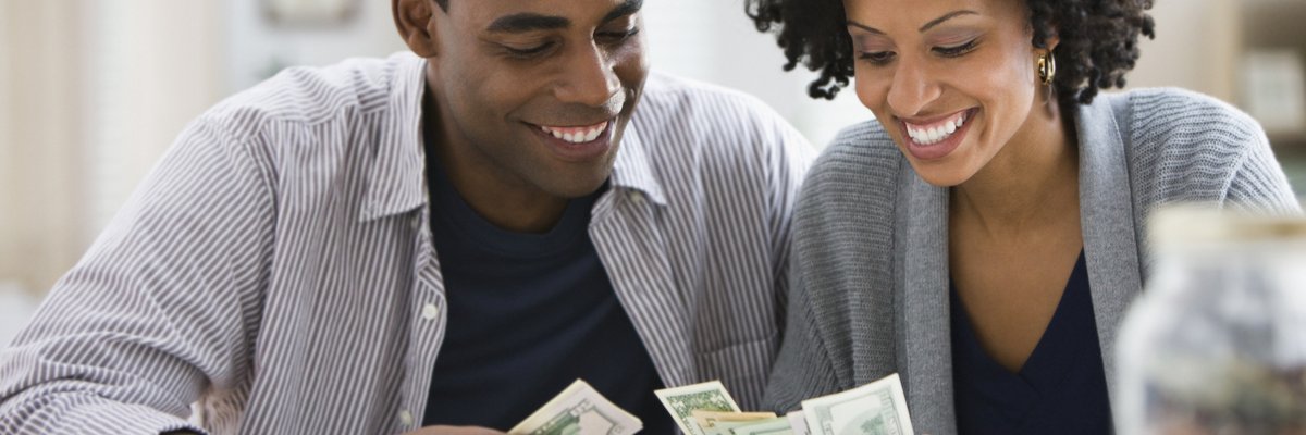 A couple counts dollar bills together at home.