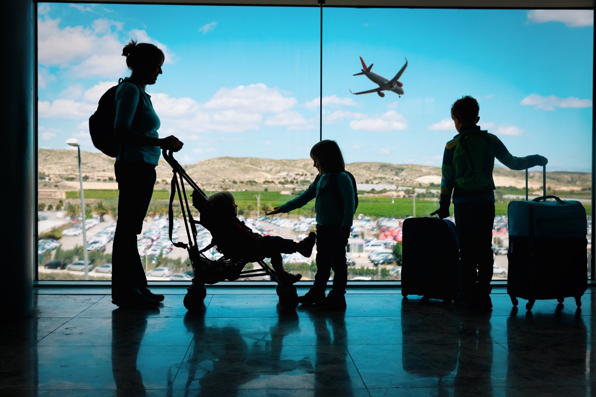 Mother with three children and luggage silhouetted in airport.
