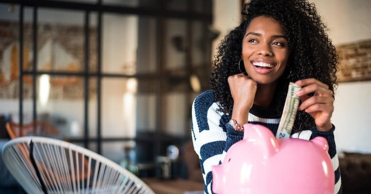 Woman puts money into a piggy bank on a table, which she is sitting by
