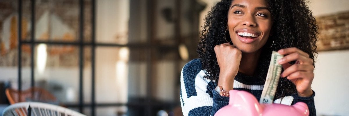 Woman puts money into a piggy bank on a table, which she is sitting by