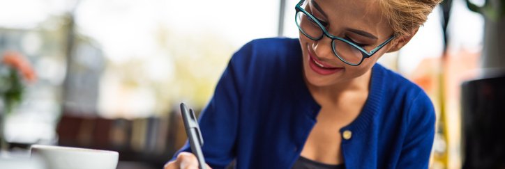Happy woman writes on paperwork at a table with a coffee cup