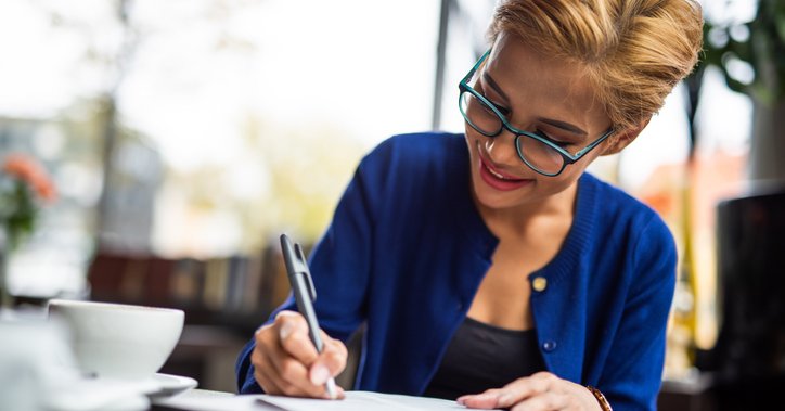 Happy woman writes on paperwork at a table with a coffee cup