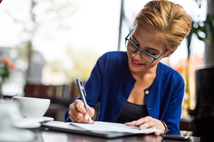Happy woman writes on paperwork at a table with a coffee cup