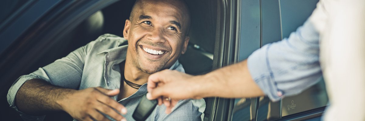 A smiling person in a car receives car keys.