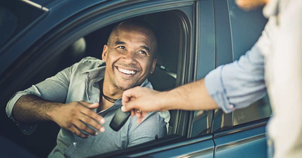 A smiling person in a car receives car keys.