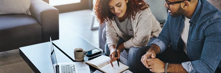 Couple discusses finances in living room with laptop and charts.