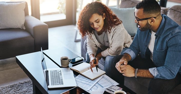 Couple discusses finances in living room with laptop and charts.