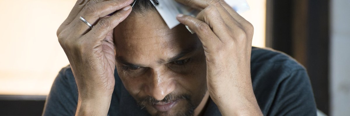Man having a mental breakdown while clutching two big fistfuls of credit cards to his head.