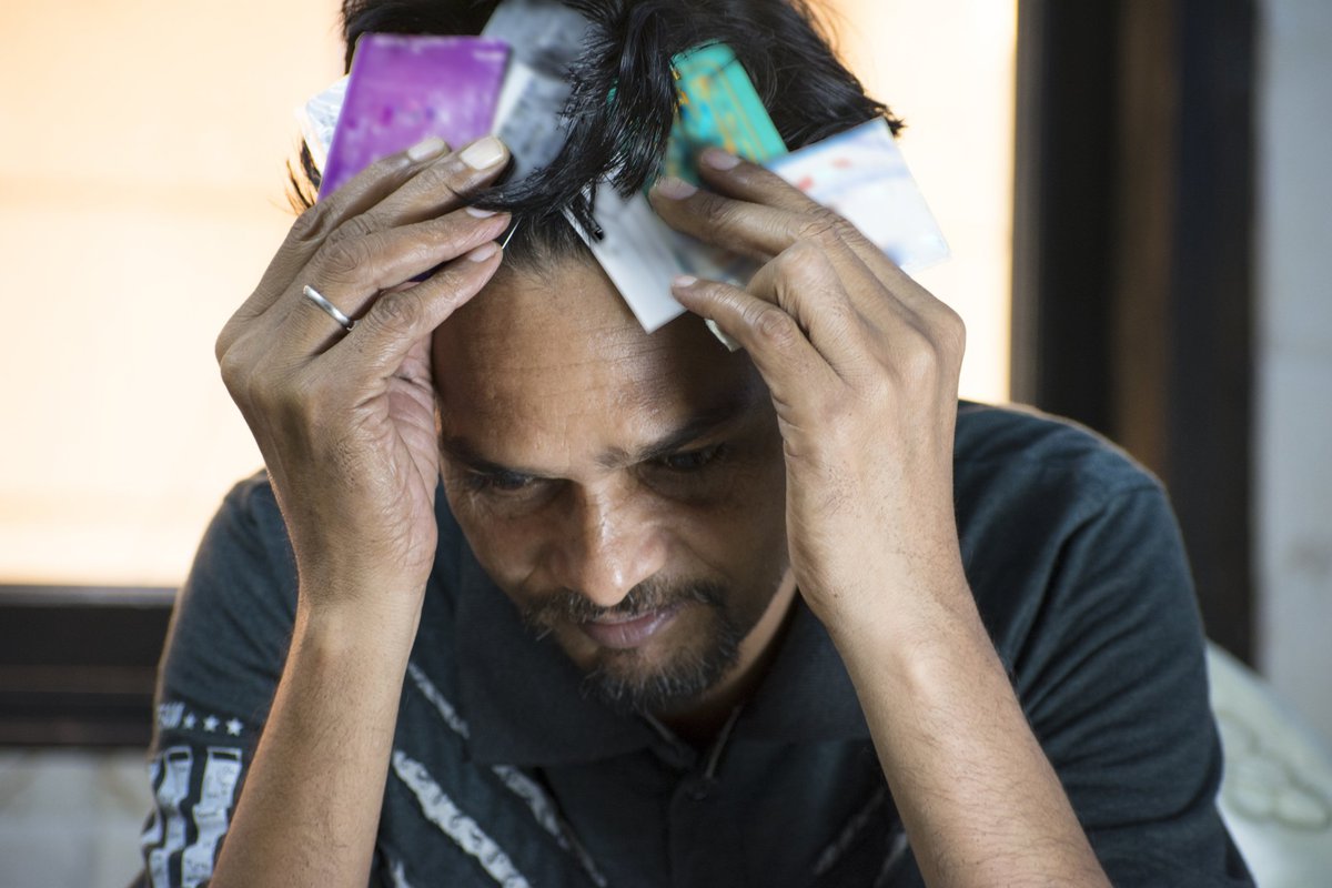 Man having a mental breakdown while clutching two big fistfuls of credit cards to his head.