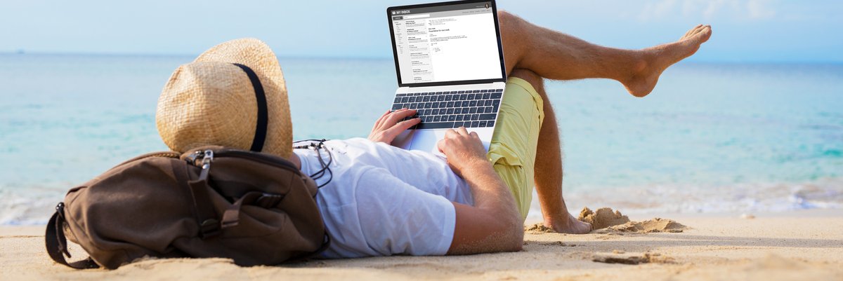 Man laying on the beach using his backpack as a pillow and with his laptop open in his lap.