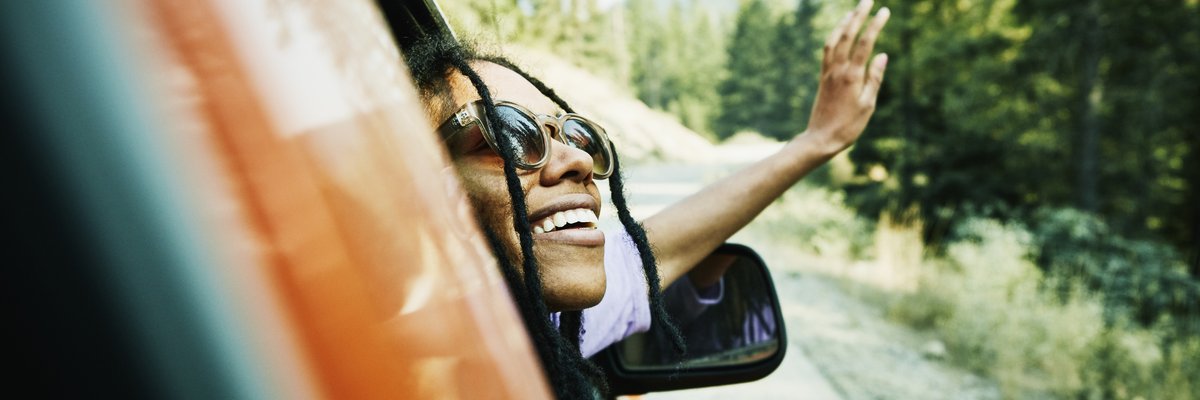 A person leans out the passenger side's window of a red car, smiling.