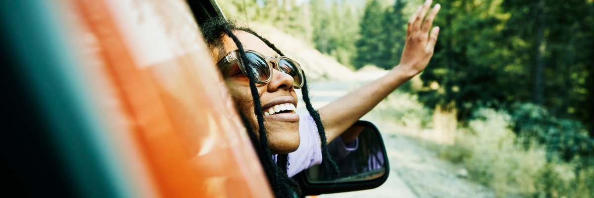 A person leans out the passenger side's window of a red car, smiling.