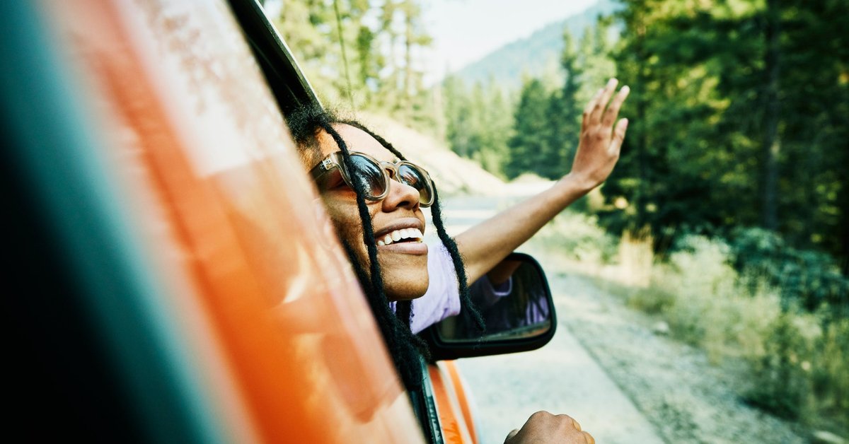 A person leans out the passenger side's window of a red car, smiling.
