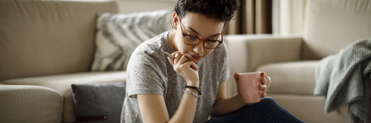 Young woman sitting on floor in front of laptop poring over bills.