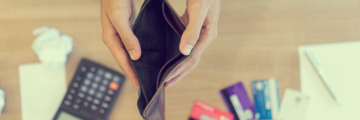 Pair of hands holding an empty wallet open over a calculator and some credit cards on a desk.