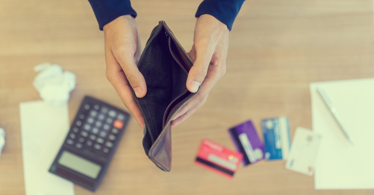 Pair of hands holding an empty wallet open over a calculator and some credit cards on a desk.