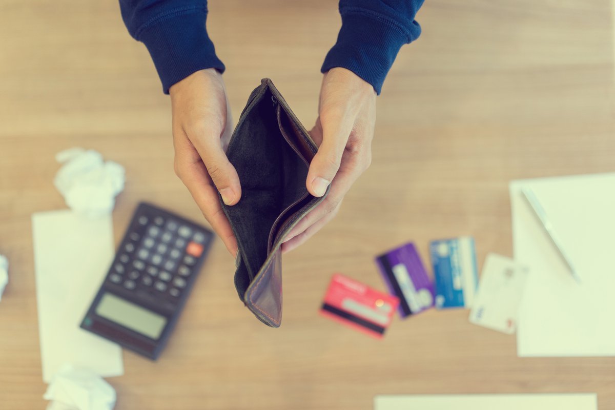 Pair of hands holding an empty wallet open over a calculator and some credit cards on a desk.