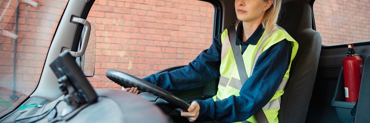 A young adult manual worker drives to work in a van wearing their uniform.
