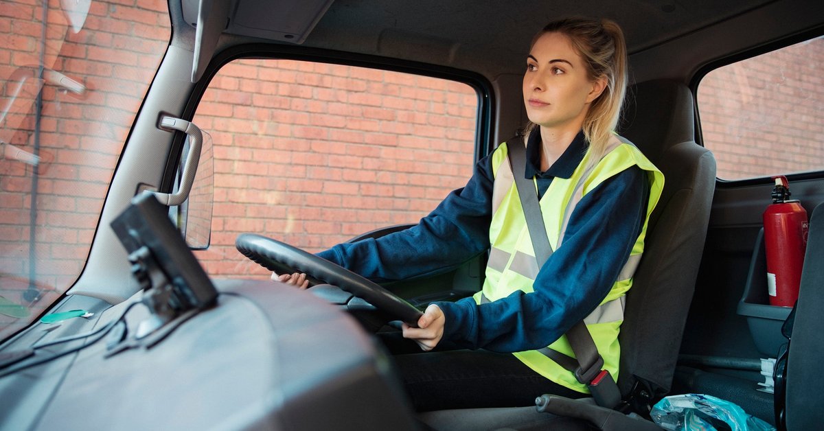 A young adult manual worker drives to work in a van wearing their uniform.