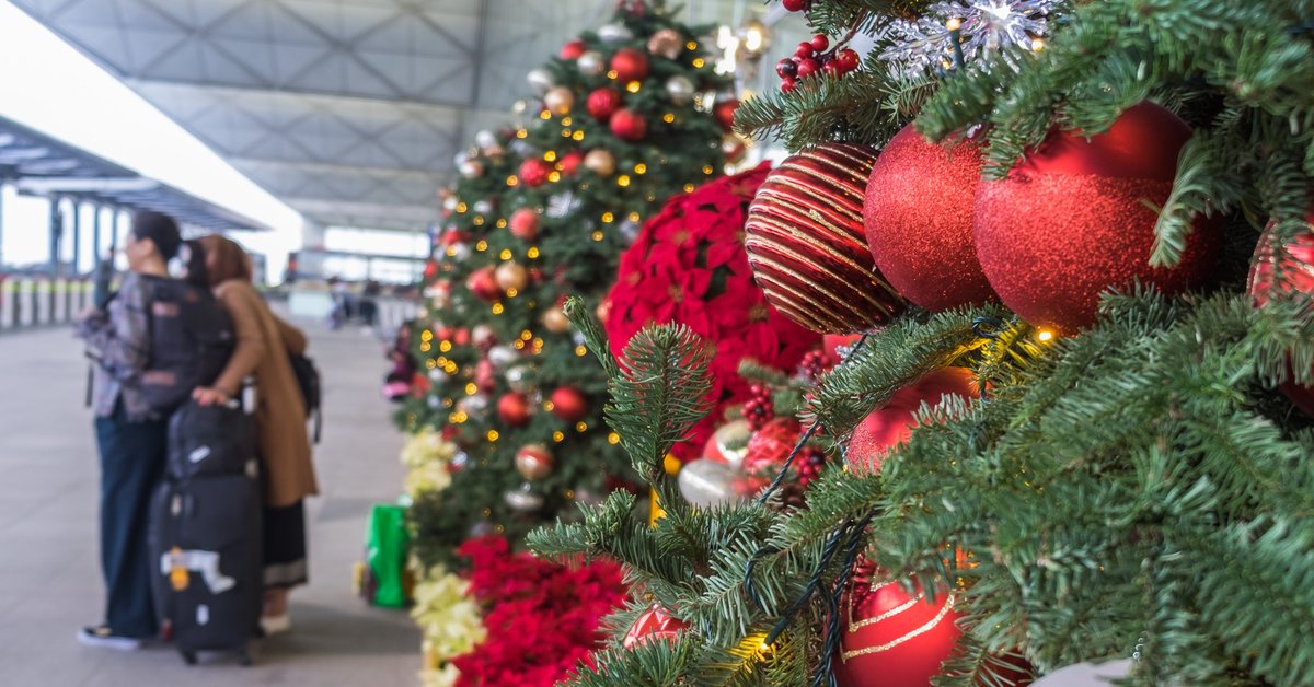 Christmas trees in airport with traveling family in background.