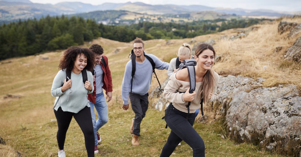A diverse pack of millennials jubilantly hike up a mountain.