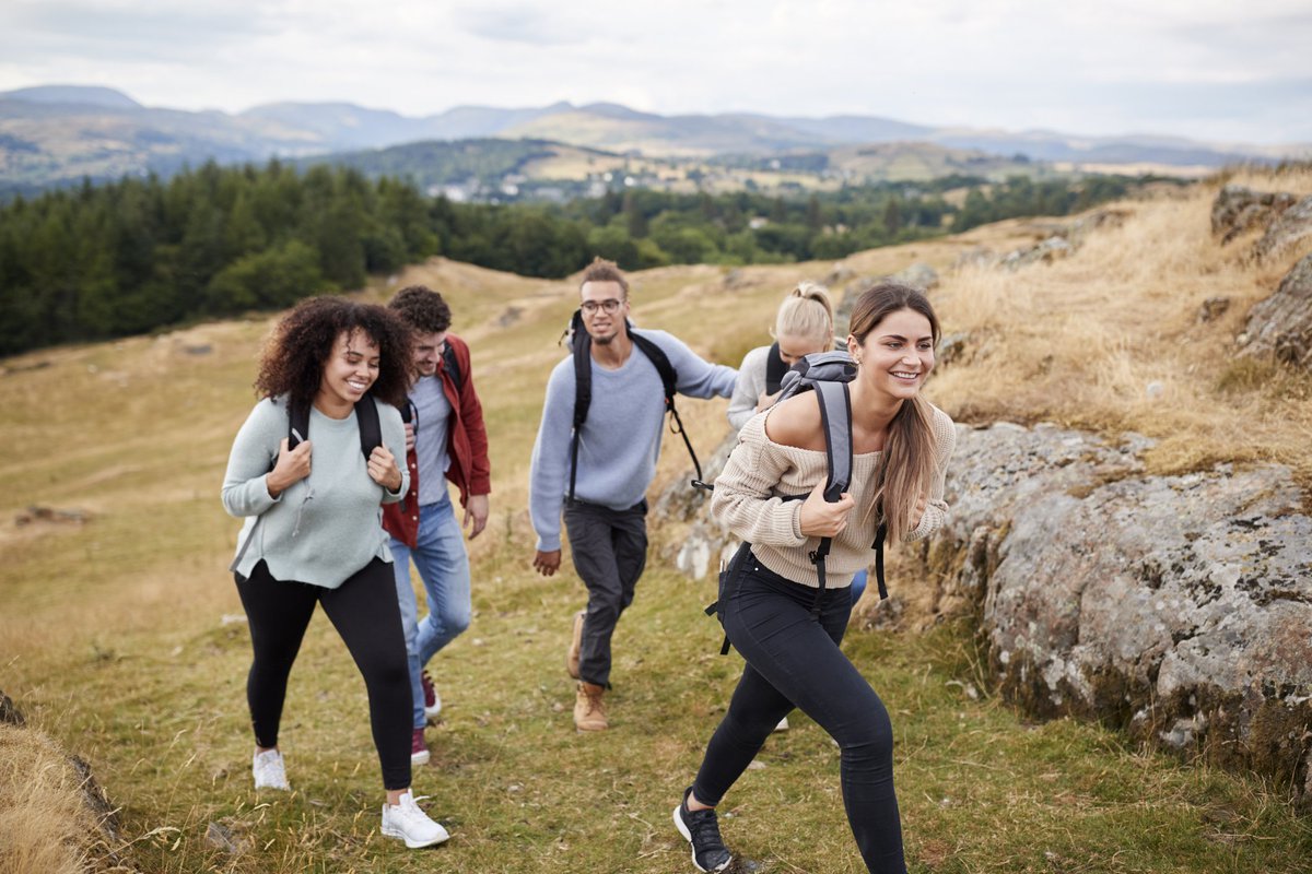 A diverse pack of millennials jubilantly hike up a mountain.
